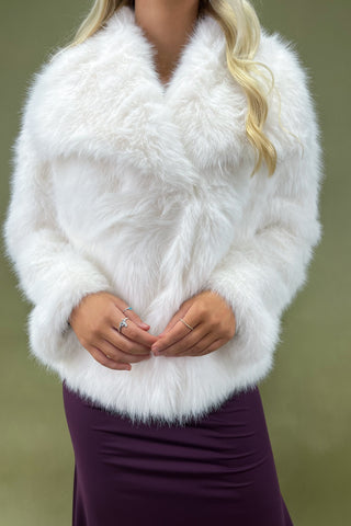 White fur shrug worn over a purple dress against a green background
