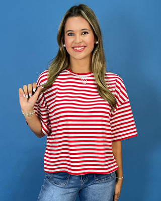 wearing a red and white horizontally striped short-sleeve t-shirt and blue jeans, posing against a solid blue background.