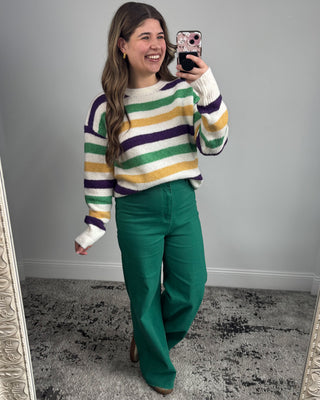 Woman taking a mirror selfie wearing a colorful striped sweater and green pants.