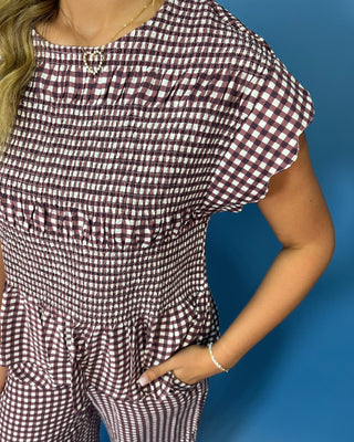 A close-up of a woman wearing a brown and white gingham smocked romper with ruffled sleeves