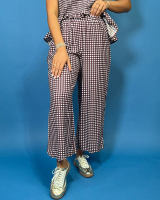 A person wearing a brown and white gingham checkered jumpsuit with wide-leg cropped pants