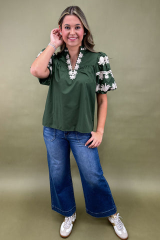 Woman wearing a green blouse with floral details and blue jeans on a green background