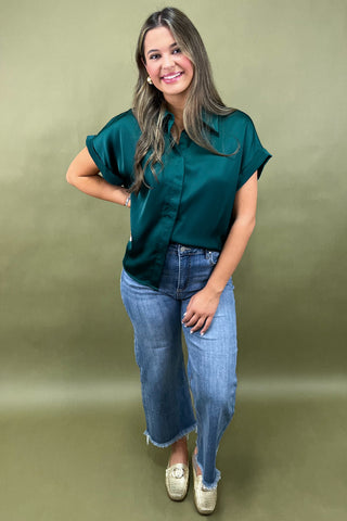 Woman wearing a teal shirt and blue jeans against a green background