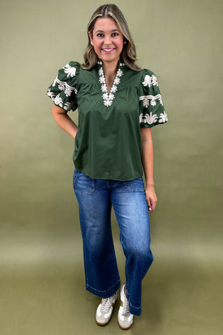 Woman wearing a green blouse with floral sleeves and blue jeans on a green background