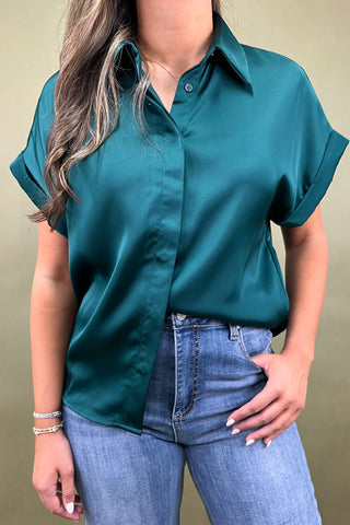 Person wearing a teal short-sleeve shirt and blue jeans against a beige background