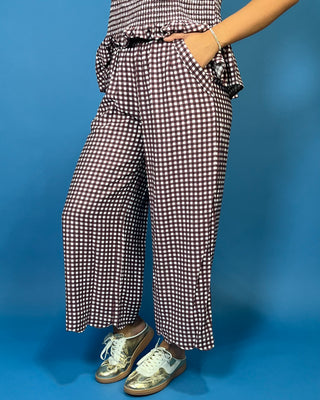 A person wearing loose, wide-leg cropped pants with a brown and white gingham check pattern