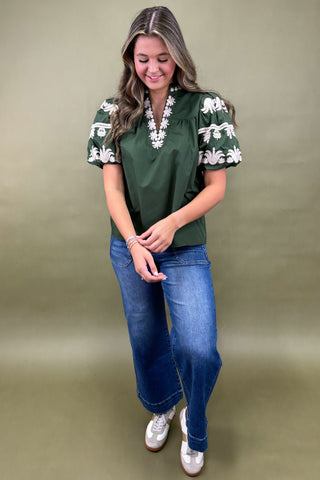 Woman wearing a green top with white floral patterns and blue jeans on a beige background
