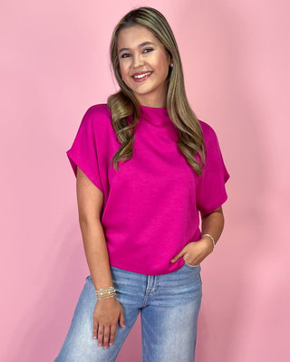 Woman wearing a bright pink top and blue jeans against a pink background