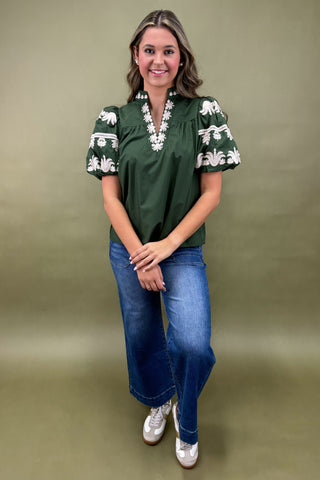 Woman wearing a green blouse with white patterns and blue jeans against a green background