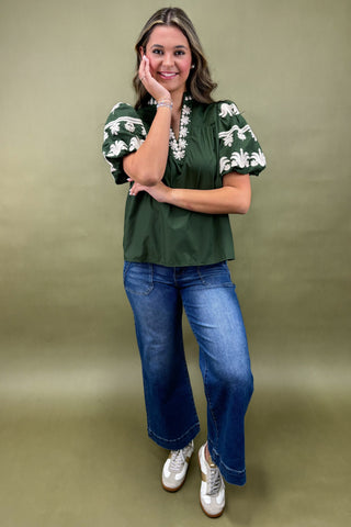 Woman wearing a green blouse with white floral patterns and blue jeans on a green background