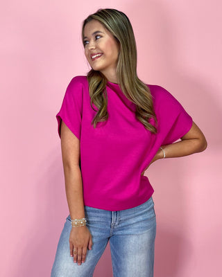 Woman wearing a bright pink top and blue jeans against a pink background