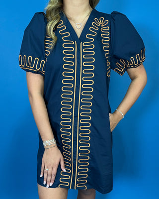 Navy short sleeve shift dress with statement puff sleeves, a flattering V-neckline, contrast tan loop trim detailing, and convenient side pockets.