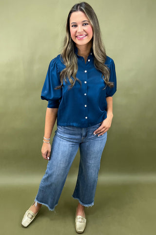 Woman wearing a blue shirt and jeans against a green background