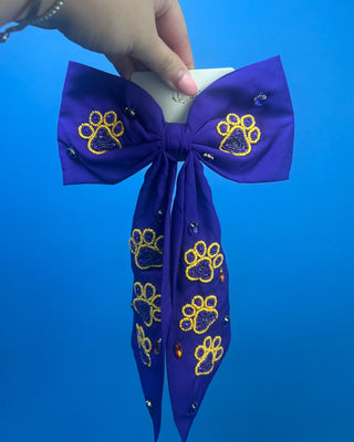 Purple LSU statement hair bow with hand-beaded gold and purple tiger paw prints, rhinestone accents, long tails, and a French barrette clip.