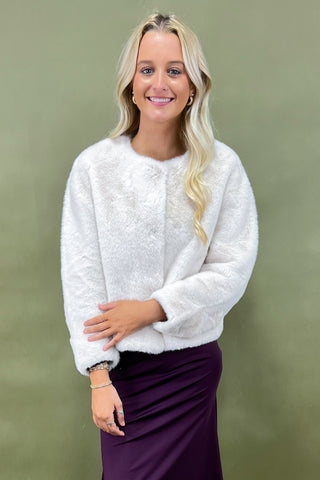 Woman wearing a white textured sweater and purple skirt against a green background