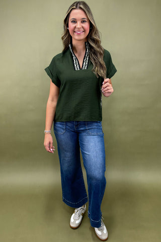 Woman wearing a green top and blue jeans against a beige background