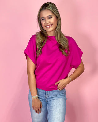 Woman wearing a bright pink top and light blue jeans against a pink background