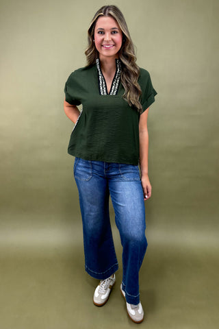 Woman wearing a green top and blue jeans against a beige background