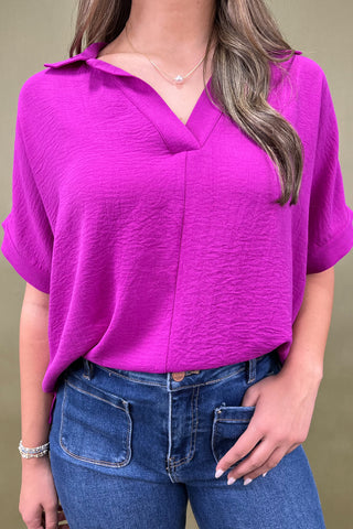 Person wearing a purple top and blue jeans against a green background