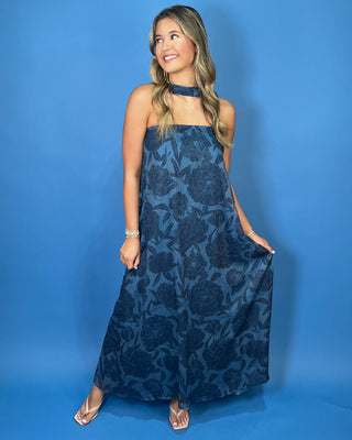 a sleeveless halter-neck maxi dress with a dark blue floral pattern on a medium blue background