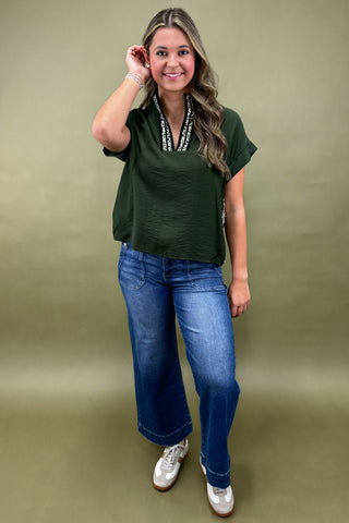 Woman wearing a green top and blue jeans against a green background