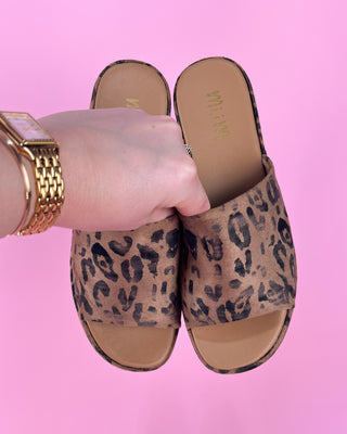 Leopard print slides held by a hand against a pink background