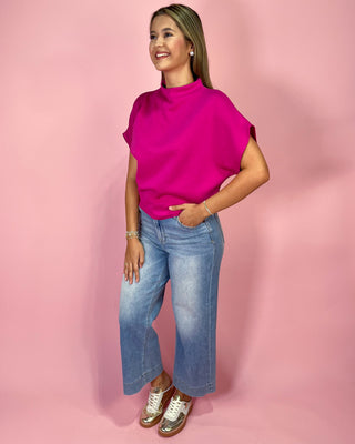 Woman wearing a bright pink top and blue jeans against a pink background