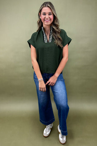 Woman wearing a green top and blue jeans against a green background