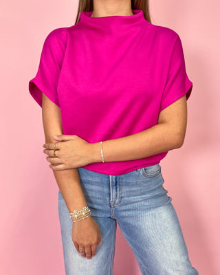 Person wearing a bright pink top and light blue jeans on a pink background