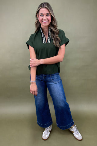 Woman wearing a green top and blue jeans against a beige background