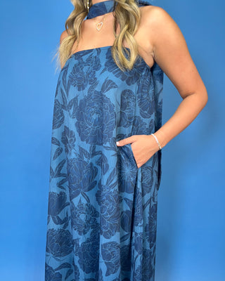 a sleeveless halter-neck maxi dress with a dark blue floral pattern on a medium blue background