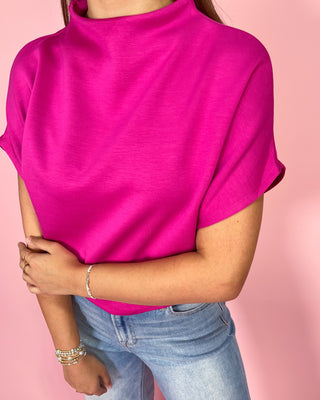 Person wearing a bright pink turtleneck and light blue jeans on a pink background