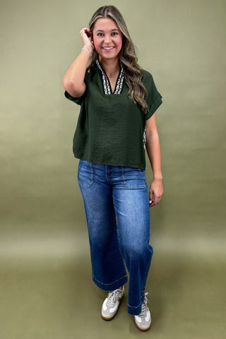 Woman wearing a green top and blue jeans against a green background