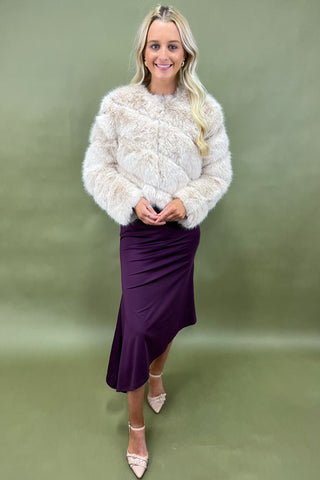 Woman wearing a white textured sweater and purple skirt against a green background