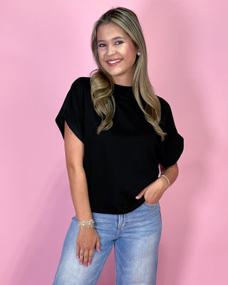 Woman wearing a black top and blue jeans against a pink background