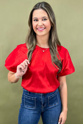 Woman wearing a red blouse and blue jeans against a green background