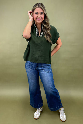 Woman wearing a green top and blue jeans against a green background
