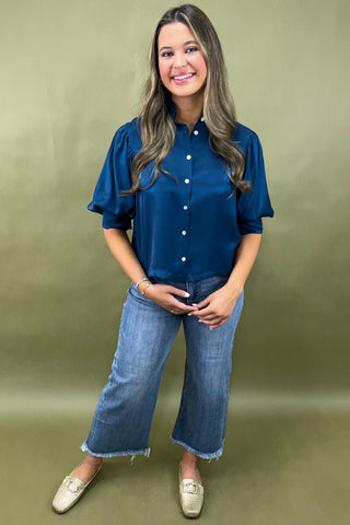 Woman wearing a blue blouse and jeans against a green background