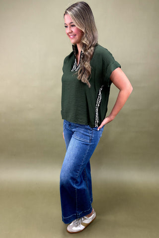 Woman wearing a green top and blue jeans against a beige background