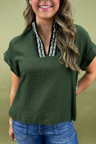 Woman wearing a green top with a decorative neckline against a beige background