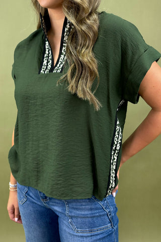 Person wearing a green top with a decorative trim and blue jeans on a green background