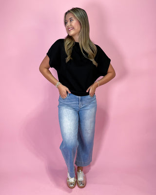 Woman wearing a black t-shirt and blue jeans against a pink background