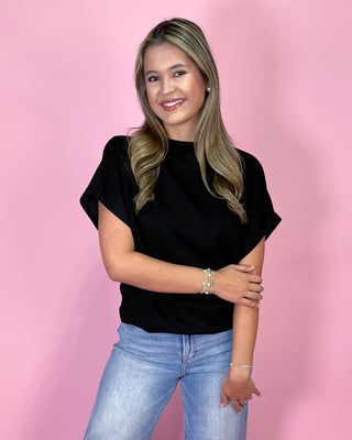 Woman wearing a black top and blue jeans against a pink background