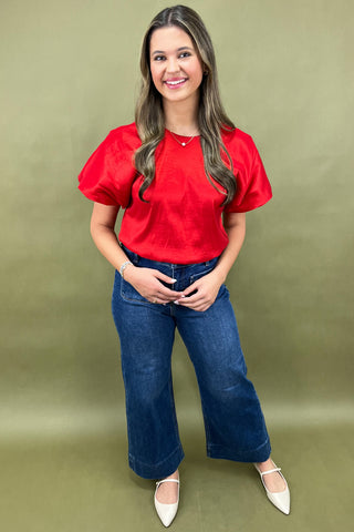Woman wearing a red blouse and blue jeans against a green background