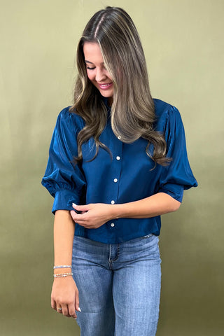 Woman wearing a blue blouse with puffed sleeves against a green background