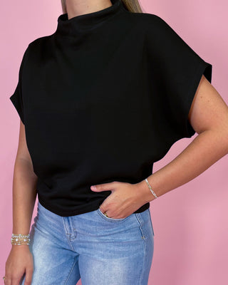 Person wearing a black sleeveless top and blue jeans against a pink background