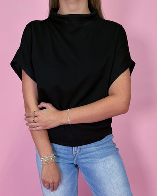Person wearing a black top and blue jeans against a pink background