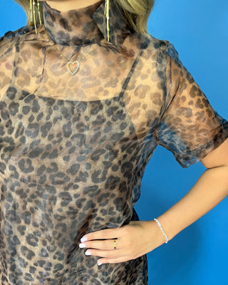 A woman modeling a sheer leopard-print midi dress with short flutter sleeves and a high mock neck