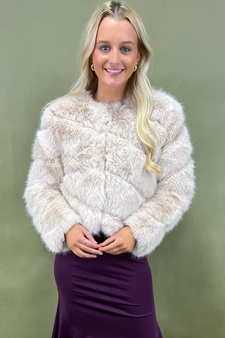 Woman wearing a fluffy beige sweater over a purple dress against a green background