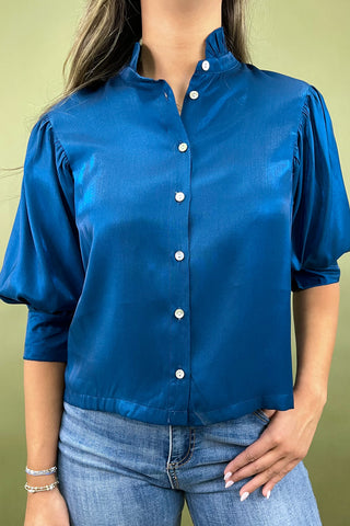 Person wearing a blue satin blouse with a green background